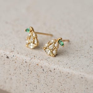 May include: A pair of gold stud earrings shaped like pears, featuring multiple clear marquise-cut stones arranged in a cluster to form the fruit body, accented with a single small green marquise-cut stone at the top to represent a leaf.