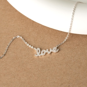 Op de afbeelding: Een delicate zilveren ketting met het woord "Love" in sierlijke letters. De letters zijn versierd met kleine, glinsterende edelstenen. De ketting is fijn en elegant, perfect voor dagelijks gebruik. Een romantisch sieraad.