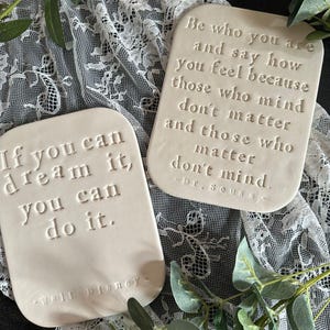 May include: Two off-white rectangular plaques with inspirational quotes. One says "If you can dream it, you can do it." by Walt Disney. The other says "Be who you are and say how you feel because those who mind don't matter and those who matter don't mind." by Dr. Seuss.