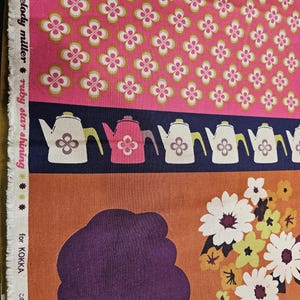 Puede incluir: Tela con un estampado floral rosa, una franja azul marino con ilustraciones de teteras y una silueta con flores. La tela tiene el texto "melody miller ruby star shining" y "for KOKKA".