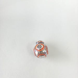 May include: A small, silver-colored BB-8 droid charm with orange and black details. The charm features a detailed design with circular and rectangular patterns, and is set against a white background.