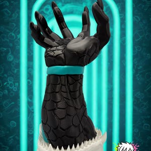 Könnte beinhalten: Eine schwarze Skulptur einer Hand mit einem strukturierten, geschuppten Arm und einem türkisfarbenen Band. Die Basis ist ein weißer Kiefer mit scharfen Zähnen. Das "MONOKREEPS"-Logo befindet sich unten rechts.