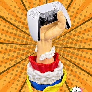 May include: A white and black PlayStation 5 controller held by a sculpted hand, rising from a tiered base of red, white, and blue. A yellow ribbon-like element curves around the base. The background is orange with a radial pattern.