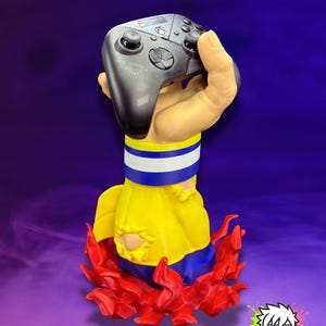 May include: A unique gaming controller holder featuring a hand holding a black controller. The holder has a yellow and blue design with red flames at the base. The logo "MONOKREEPS" is visible.