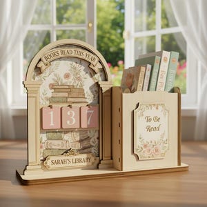 May include: A wooden bookshelf and reading tracker with the text "BOOKS READ THIS YEAR" and "SARAH'S LIBRARY". It has a floral design and a counter showing "137". The right side is labeled "To Be Read" and holds books.
