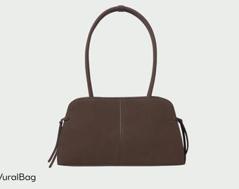 May include: A brown handbag with a rectangular body and arched handles. The bag has a vertical seam down the center and decorative ties on each side. The brand name "VuralBag" is at the bottom left.