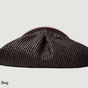 Könnte beinhalten: Dunkelbraune Clutch-Tasche mit gewebter Textur. Die Tasche hat einen geschwungenen, dunkelbraunen Griff oben. Der Text "Vural Bag" befindet sich unten im Bild.