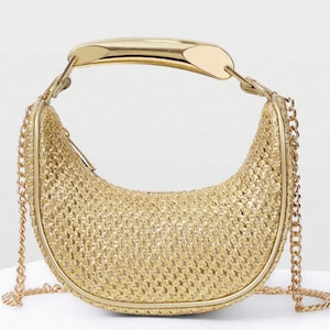 Puede incluir: Un bolso dorado en forma de media luna con una textura tejida. El bolso presenta un asa dorada y correas de cadena. El diseño es moderno y elegante, adecuado para diversas ocasiones.
