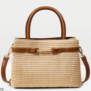 Puede incluir: Un bolso de mano de paja tejida con asas y detalles de cuero marrón. El bolso tiene forma rectangular con un asa superior y una correa de hombro desmontable. Un cierre metálico dorado asegura la parte delantera. El bolso es de color neutro.