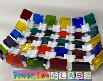 May include: A colorful glass dish with a woven design. The dish features squares of red, yellow, blue, green, and white glass. The base of the dish has the text "Peace Luv GLASS".