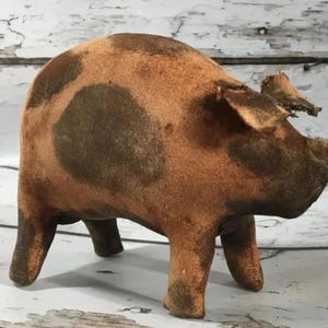 Peut inclure: Figurine de cochon de style vintage dans les tons marron et beige. Le cochon a des taches brun foncé sur le corps et se tient sur quatre courtes pattes. Les oreilles sont légèrement déchirées, ce qui lui donne un aspect rustique.