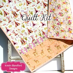 May include: A quilt kit featuring a pink, white, and green fabric with a pattern of tipis, boots, and arrows. The fabric is folded in half, and the text "Quilt Kit" is visible in the center of the image. The back of the quilt is a peach color with a floral pattern.