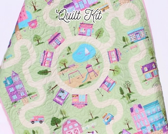May include: A green and white quilt kit featuring a whimsical town design with houses, shops, a park, and a horse farm. The quilt kit includes the text "Quilt Kit".