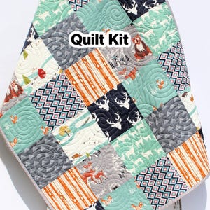 May include: A patchwork quilt kit with a variety of patterns and colors. The quilt features squares with deer, foxes, and geometric designs in shades of teal, gray, orange, and navy. The text "Quilt Kit" is visible.
