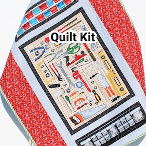 May include: A quilt kit featuring a tool-themed fabric with a variety of tools, including hammers, wrenches, screwdrivers, and saws. The fabric is surrounded by a red and white border with a green and white trim. The quilt kit is labeled "Quilt Kit" and "Kristin Blandford Designs".