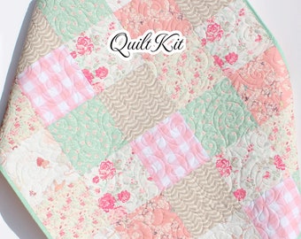 May include: A patchwork quilt with a pink, green, and brown color scheme. The quilt is made of various floral and gingham fabrics. The quilt is folded and displayed on a white wooden ladder. The text "Quilt Kit" is visible in the center of the quilt. The text "Kristin Blandford Designs" is visible in the lower right corner of the image.