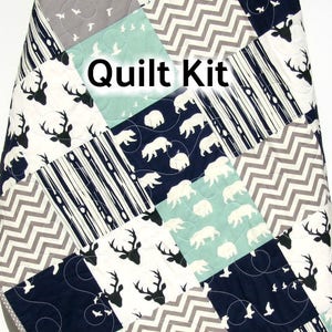 May include: A quilt kit featuring a variety of fabrics with woodland animal prints, including deer, bears, and birds. The fabrics are in shades of blue, gray, and white. The text "Quilt Kit" is visible in the center of the image.