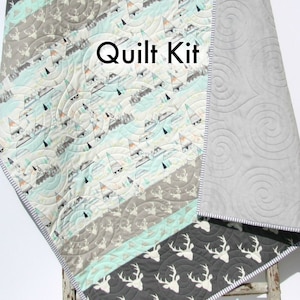 May include: A quilt kit featuring a gray and white deer print fabric, a light blue and white fabric with a geometric pattern, and a gray fabric with a swirl pattern. The kit includes the text "Quilt Kit" and "Kristin Blandford Designs".