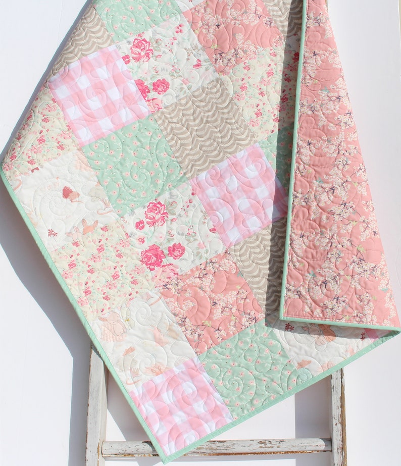 Puede incluir: Una colcha de beb&eacute; de retazos con un borde verde. La colcha est&aacute; hecha de varias telas florales y vichy en tonos de rosa, verde y blanco.