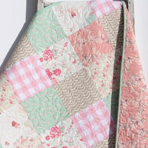 Puede incluir: Una colcha de retazos con un patr&oacute;n floral verde, rosa y blanco. La colcha est&aacute; hecha de diferentes telas y tiene un borde festoneado.