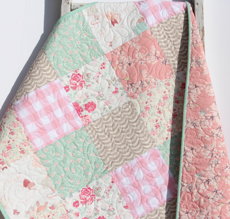 Puede incluir: Una colcha de retazos con un patr&oacute;n floral verde, rosa y blanco. La colcha est&aacute; hecha de diferentes telas y tiene un borde festoneado.