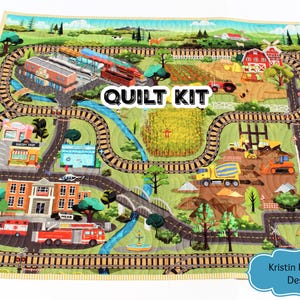 May include: A colorful quilt kit featuring a town and farm scene with roads, train tracks, and buildings. The quilt includes a fire station, bakery, and farm with a red barn. The words "QUILT KIT" are displayed on the quilt.