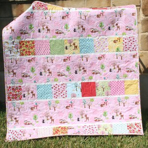 Beginner-friendly charm pack quilt pattern with pink woodland fabrics, novelty prints, and crisp white sashing in a modern baby quilt layout.