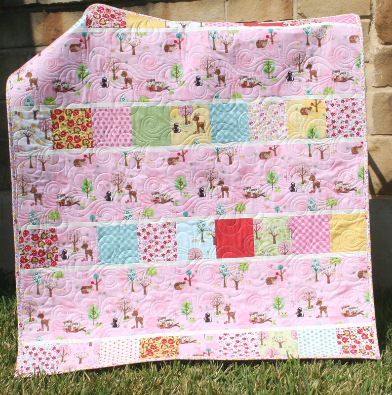 Beginner-friendly charm pack quilt pattern with pink woodland fabrics, novelty prints, and crisp white sashing in a modern baby quilt layout.