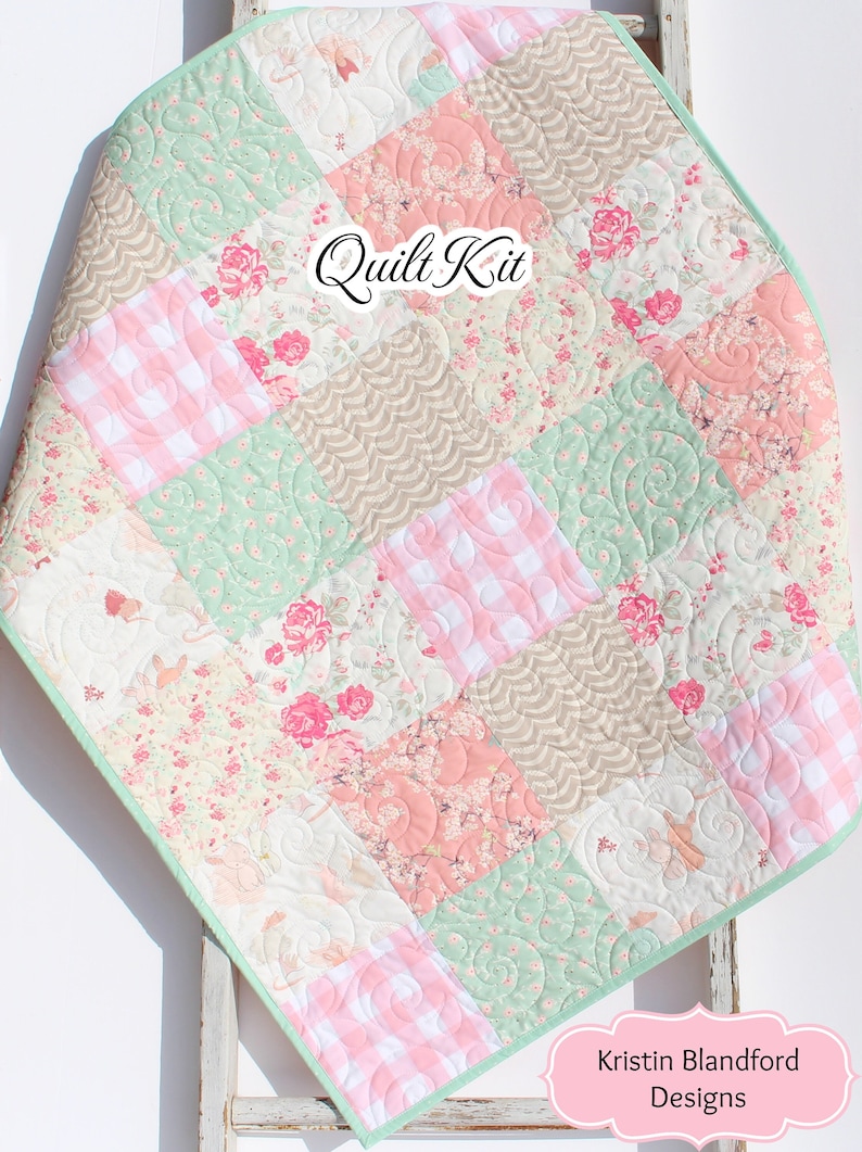 Puede incluir: Una colcha de retazos con un esquema de color rosa, verde y marr&oacute;n. La colcha est&aacute; hecha de varias telas florales y de cuadros. La colcha est&aacute; doblada y expuesta en una escalera de madera blanca. El texto "Quilt Kit" es visible en el centro de la colcha. El texto "Kristin Blandford Designs" es visible en la esquina inferior derecha de la imagen.