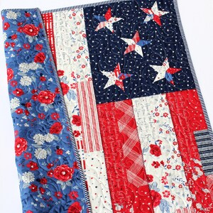 May include: A red, white, and blue patchwork quilt with a floral pattern on the back. The front of the quilt features a traditional American flag design with stars and stripes. The quilt is quilted with a swirling pattern.