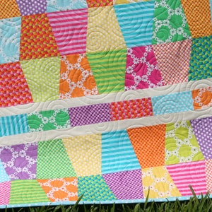 Easy charm pack quilt pattern featuring a modern tumbling block effect with colorful geometric piecing and crisp white sashing. This downloadable PDF quilt pattern by Kristin Blandford Designs is designed for baby quilts and throw quilts and works beautifully with precut charm packs, coordinated fabric collections, or scrap fabrics.
