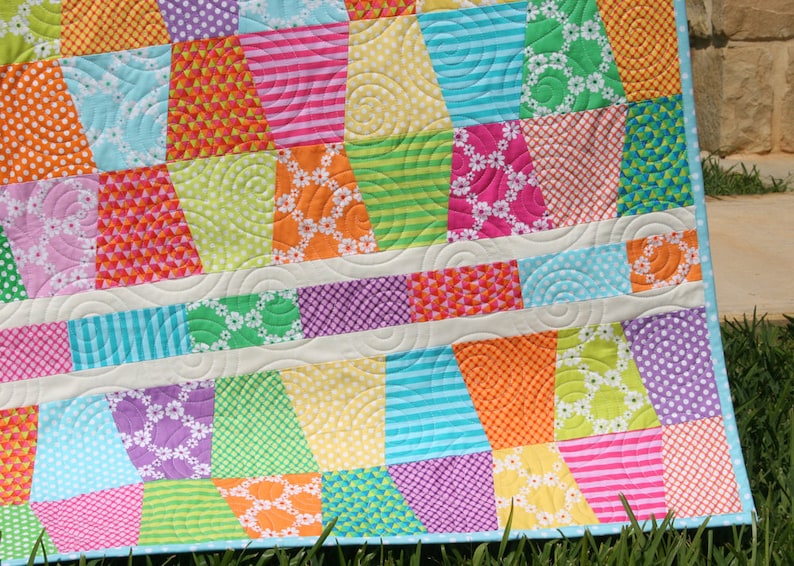 Easy charm pack quilt pattern featuring a modern tumbling block effect with colorful geometric piecing and crisp white sashing. This downloadable PDF quilt pattern by Kristin Blandford Designs is designed for baby quilts and throw quilts and works beautifully with precut charm packs, coordinated fabric collections, or scrap fabrics.