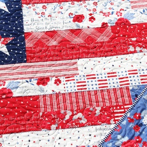 May include: A red, white, and blue patchwork quilt with a patriotic theme. The quilt is made of different fabrics with stars, stripes, and floral patterns. The quilt is quilted with a swirl pattern. The text "Stars & Stripes Home of the Free Justice Freedom for Freedom Land of the Brave Stars & Stripes Land of the Brave" is visible on the quilt.