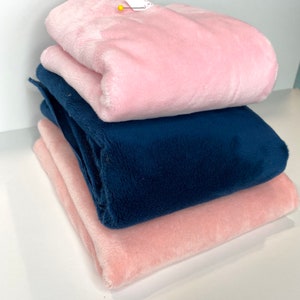 May include: A stack of three plush blankets in shades of pink and navy blue. The blankets are folded neatly, showcasing their soft, fluffy texture. A small tag is pinned to the top blanket.