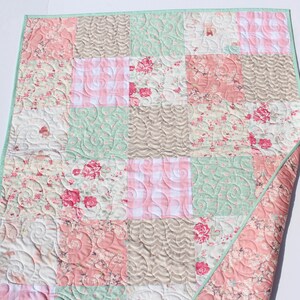 Puede incluir: Una colcha de retazos con un patr&oacute;n floral y vichy en tonos rosa, verde y marr&oacute;n. La colcha est&aacute; acolchada con un dise&ntilde;o de espiral.