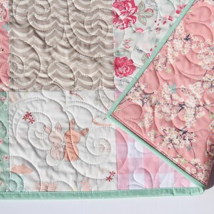 Puede incluir: Una colcha de beb&eacute; de retazos con una variedad de estampados florales y de animales. La colcha est&aacute; hecha con colores suaves y pastel y tiene un ribete verde claro. La colcha est&aacute; acolchada con un patr&oacute;n de espiral.