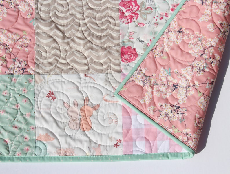 Puede incluir: Una colcha de beb&eacute; de retazos con una variedad de estampados florales y de animales. La colcha est&aacute; hecha con colores suaves y pastel y tiene un ribete verde claro. La colcha est&aacute; acolchada con un patr&oacute;n de espiral.
