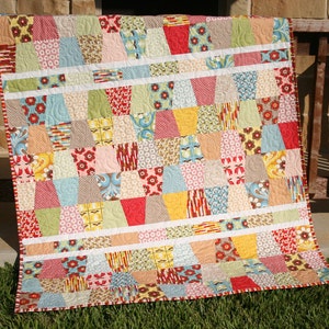 Fun and easy Tumbled quilt pattern featuring bright rainbow inspired patchwork blocks made from charm pack squares and precut quilting fabrics. This digital PDF sewing pattern by Kristin Blandford Designs is beginner friendly and ideal for fast quilt finishes, colorful baby blankets, and modern throw quilt projects.