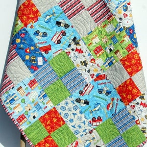 A colorful patchwork quilt with a blue, red, and green color scheme. The quilt features a variety of images, including fire trucks, police cars, and helicopters. The quilt is made with a variety of fabrics and textures, and is perfect for a child's room.