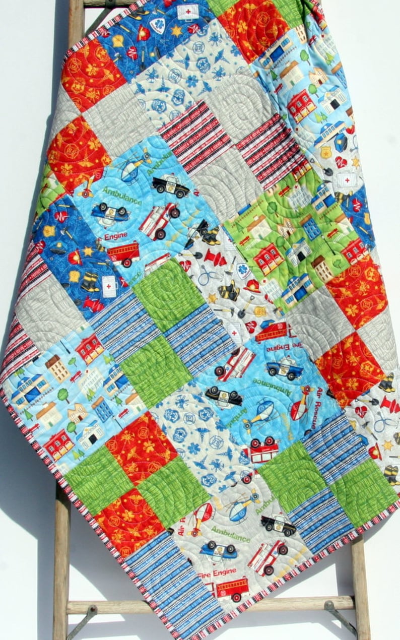 A colorful patchwork quilt with a blue, red, and green color scheme. The quilt features a variety of images, including fire trucks, police cars, and helicopters. The quilt is made with a variety of fabrics and textures, and is perfect for a child's room.