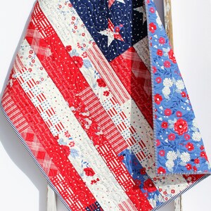 May include: A red, white, and blue patchwork quilt with a star pattern on the blue section. The quilt is folded and draped over a white wooden ladder.