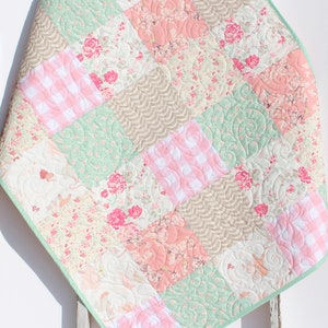 Puede incluir: Una colcha de beb&eacute; de patchwork con un esquema de color verde, rosa y marr&oacute;n. La colcha est&aacute; hecha de varias telas florales y de cuadros.
