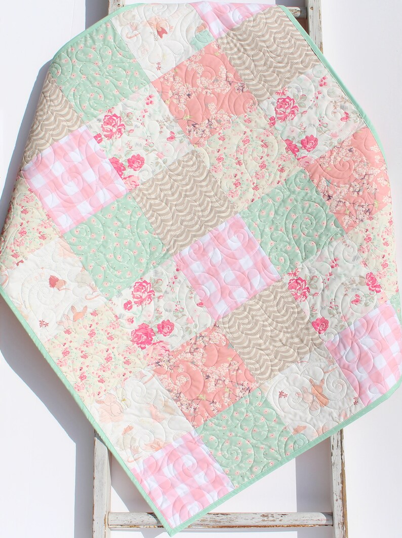 Puede incluir: Una colcha de beb&eacute; de patchwork con un esquema de color verde, rosa y marr&oacute;n. La colcha est&aacute; hecha de varias telas florales y de cuadros.