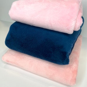 May include: Three plush blankets stacked on top of each other. The top blanket is pink, the middle blanket is navy blue, and the bottom blanket is pink.