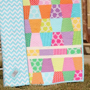 Modern patchwork quilt pattern with colorful tumbling blocks and white horizontal sashing designed for charm pack fabrics and beginner quilters. This PDF quilt pattern by Kristin Blandford Designs is perfect for creating bright baby quilts, lap throws, nursery quilts, and handmade gifts with bold modern fabric collections.