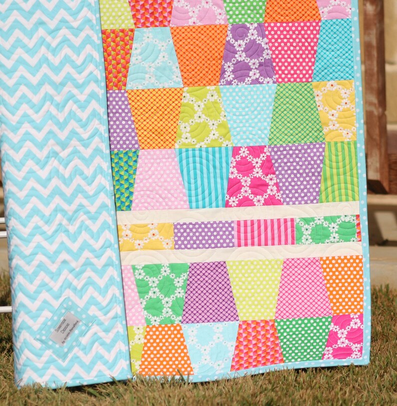 Modern patchwork quilt pattern with colorful tumbling blocks and white horizontal sashing designed for charm pack fabrics and beginner quilters. This PDF quilt pattern by Kristin Blandford Designs is perfect for creating bright baby quilts, lap throws, nursery quilts, and handmade gifts with bold modern fabric collections.