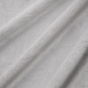 May include: Close-up of a soft, light gray fabric with a fuzzy texture. The fabric is folded and has a subtle sheen.