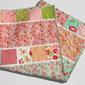 A patchwork quilt with a variety of floral patterns in pink, green, and white. The quilt is made of squares and rectangles, and the edges are finished with a light blue binding.