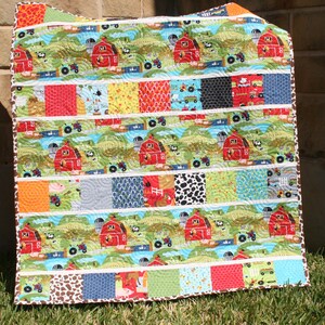 Easy farm baby quilt pattern using novelty barnyard fabrics and colorful charm square patchwork strips in a beginner-friendly design.