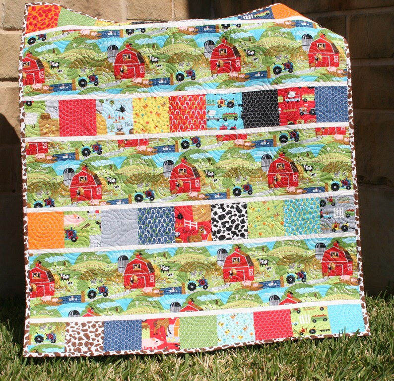 Easy farm baby quilt pattern using novelty barnyard fabrics and colorful charm square patchwork strips in a beginner-friendly design.